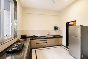A modern kitchen with a gas stove, a refrigerator, and a microwave. - Alaya Stays Riva Amar Villa 3BHK (Udaipur)