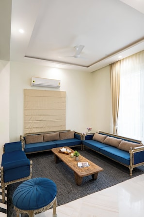 A modern living room with a sectional sofa, a wooden coffee table, and a ceiling fan. - Alaya Stays Riva Amar Villa 3BHK (Udaipur)