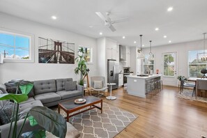 A modern living room with a grey sofa, a coffee table, and a dining area with bar stools.
