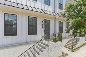 A residential building with a brick facade, multiple windows with shutters, and a staircase leading to the entrance.