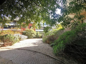 Un chemin pavé aménagé dans un espace paysager, avec un feuillage dense et un bâtiment en arrière-plan.