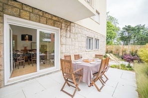 Une terrasse extérieure avec une table dressée pour le repas, entourée de murs en pierre et une porte vitrée donnant sur un espace de salle à manger intérieur.