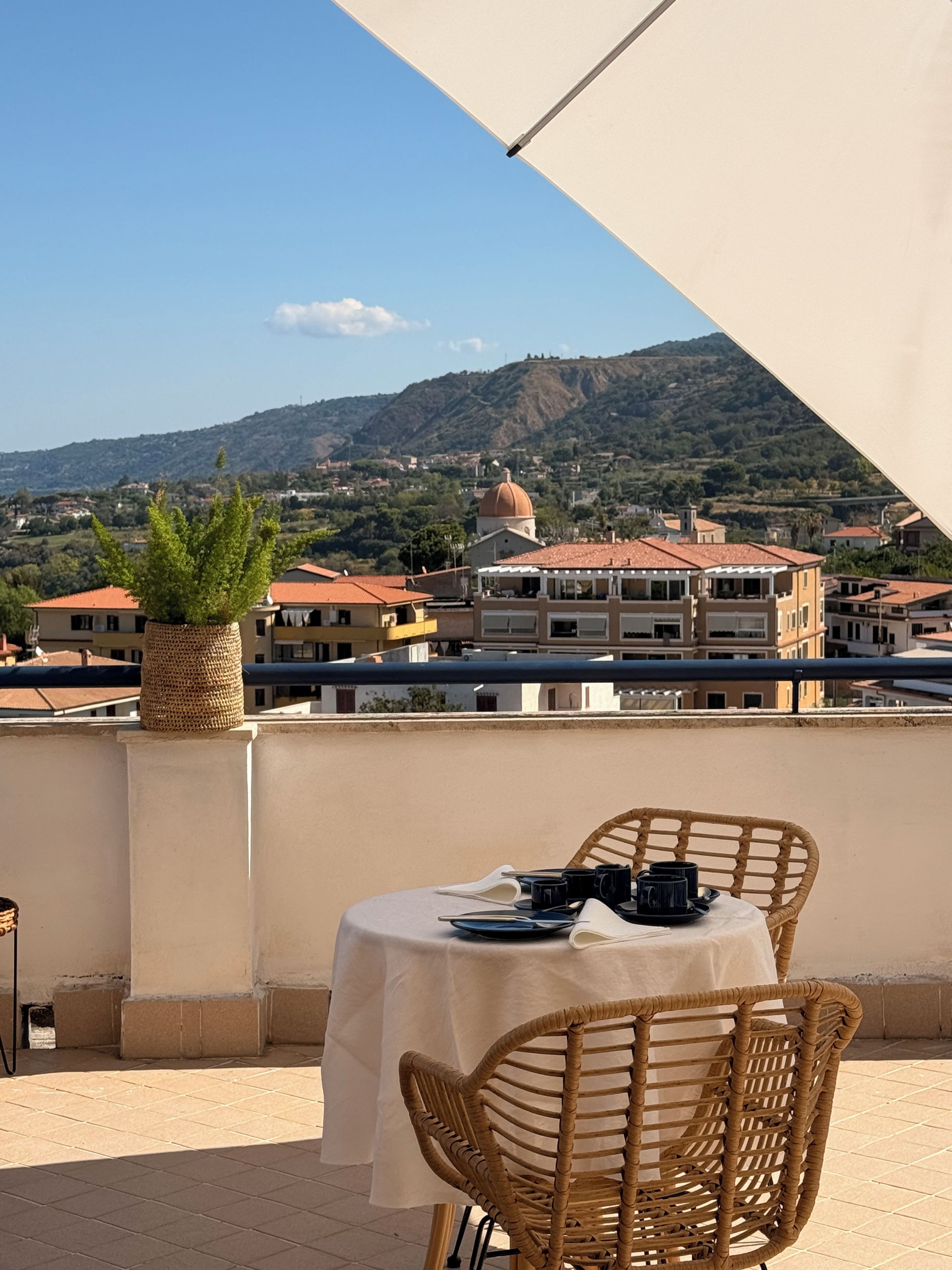 A terrace with a table set for two, overlooking a town with buildings and a hill.