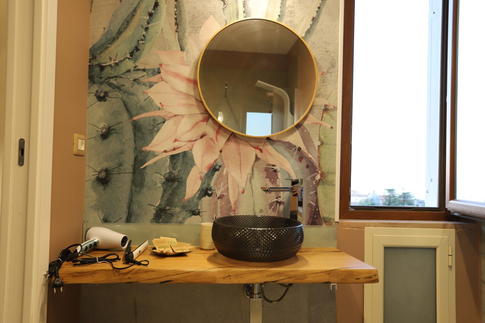 A bathroom with a wooden vanity, a round mirror, a textured basin, and a floral wall mural.