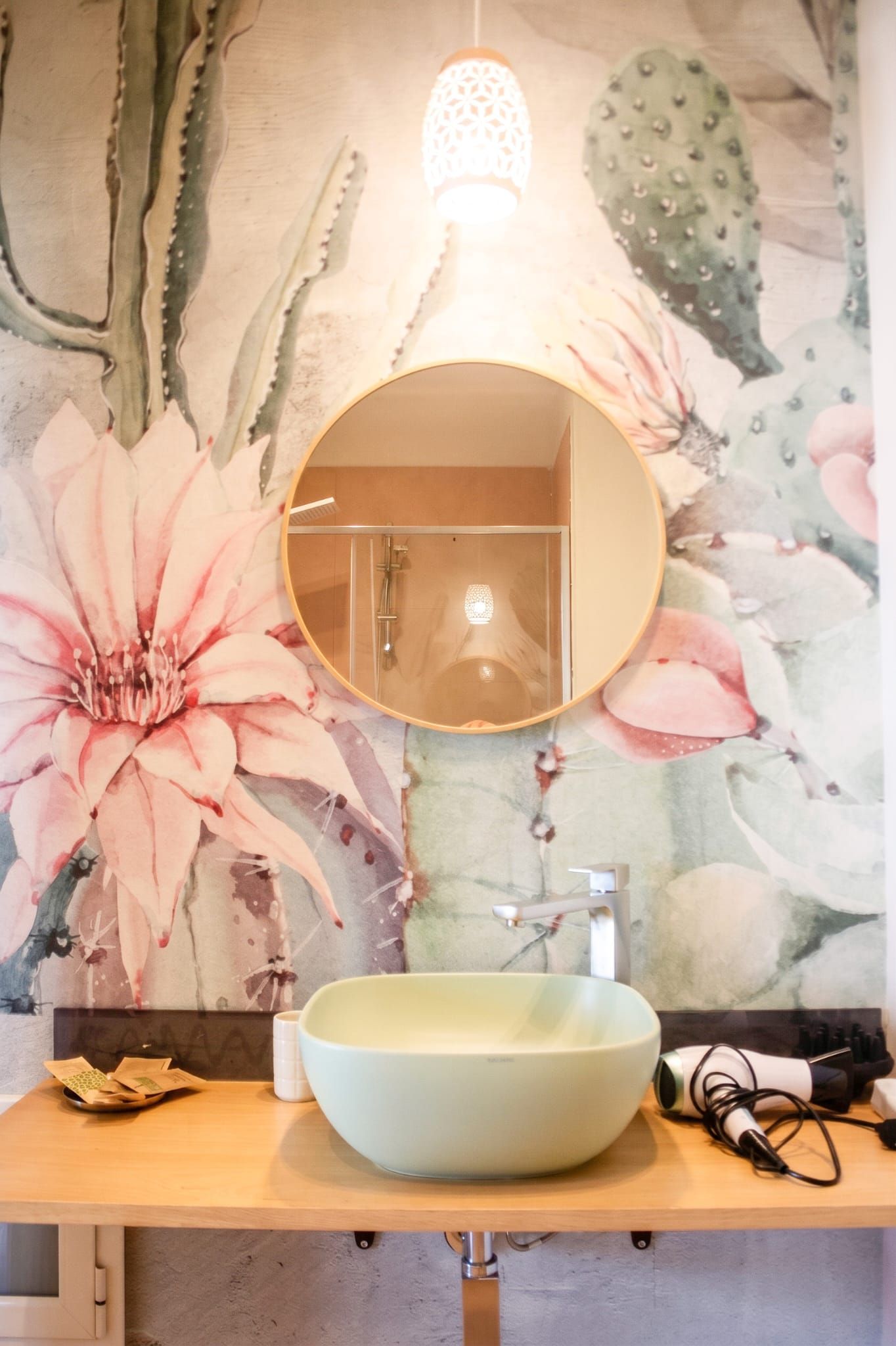 A bathroom with a round mirror, a light fixture, and a floral wall mural.