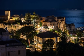 Un pueblo costero nocturno con edificios iluminados, una torre de iglesia destacada y un litoral rocoso.