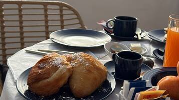 A breakfast setup with croissants on a plate, a coffee cup, a glass of orange juice, and a book holder on a table.
