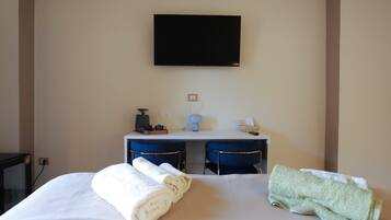 Una habitación de hotel con una cama, dos sillas, un escritorio, un televisor y una cafetera.