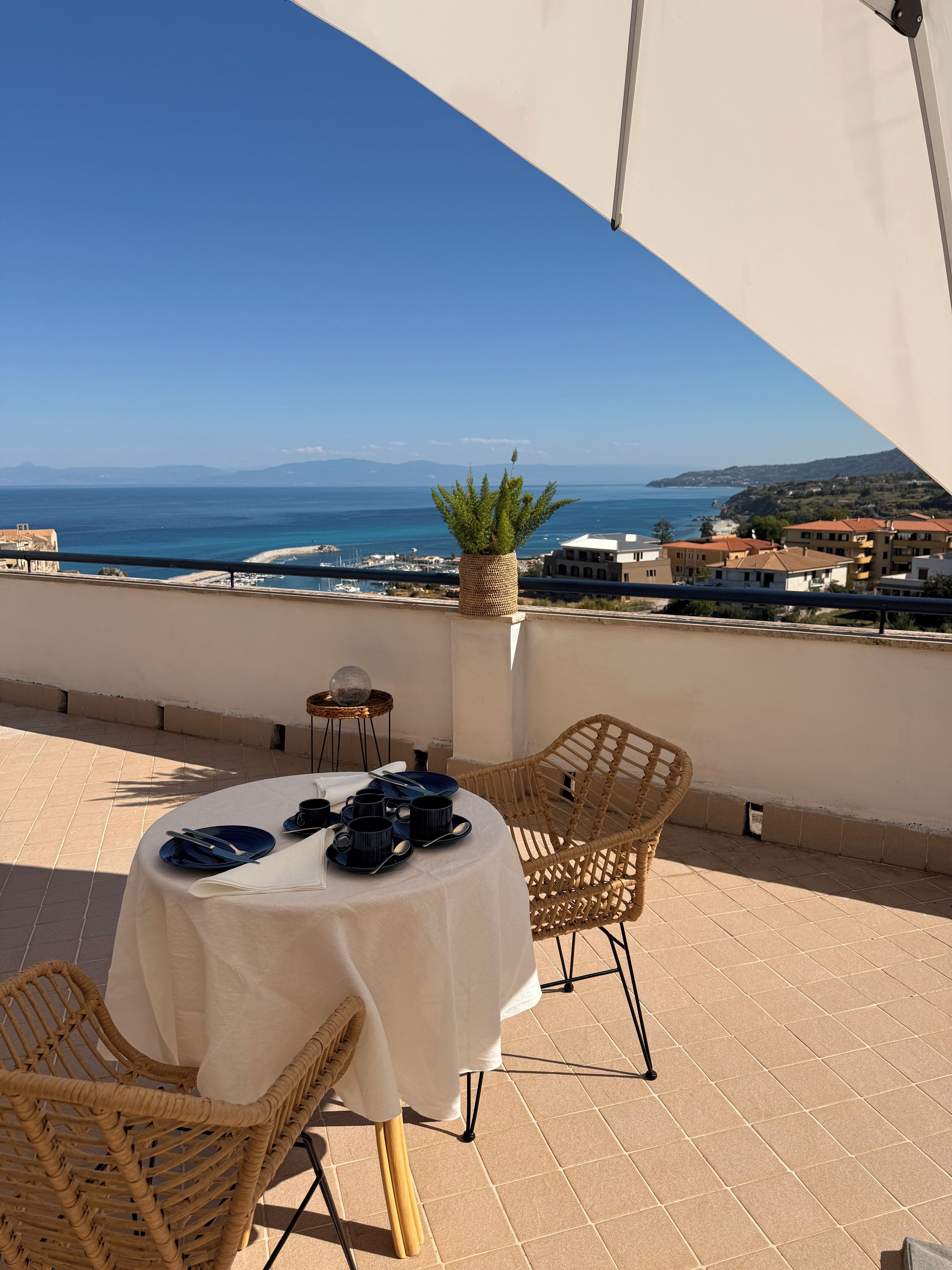A terrace with a table set for dining, overlooking a coastal view.