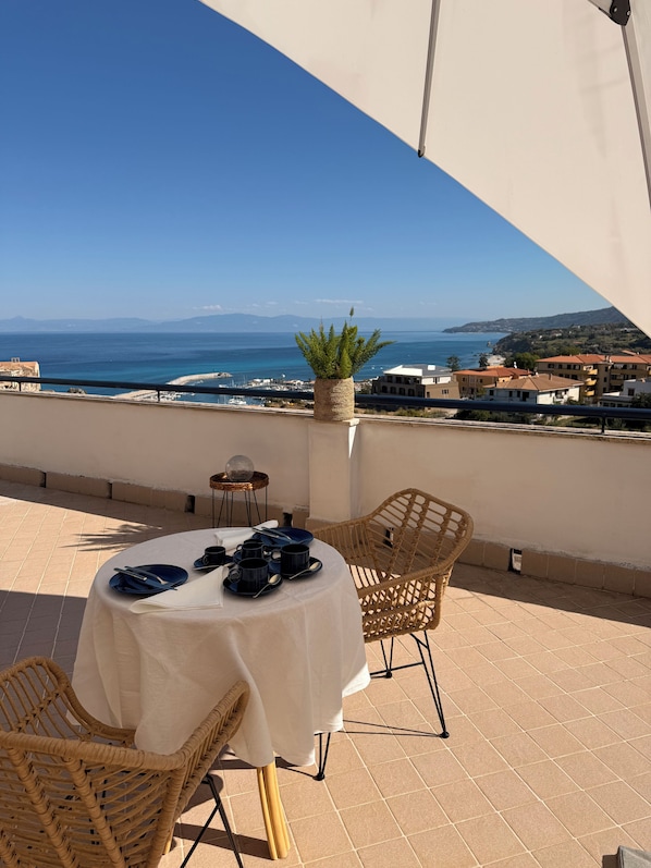 A terrace with a table set for dining, overlooking a coastal view.