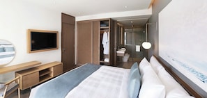 Ein modernes Hotelzimmer mit Bett, Fernseher, Schreibtisch, Kleiderschrank und einem durchgegangenen Tür sichtbaren Badezimmer.