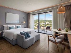 Ein modernes Hotelzimmer mit einem großen Bett, einer Couch, einem Esstisch und Blick ins Freie.