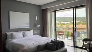 Ein Schlafzimmer mit einem großen Bett, Blick ins Freie und einem Balkon mit Stühlen.