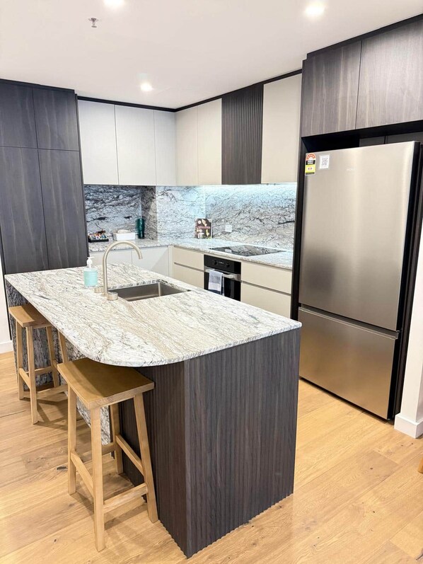 Eine moderne Küche mit Marmorarbeitsplatte, Edelstahlgeräten und Holzbarhocker.