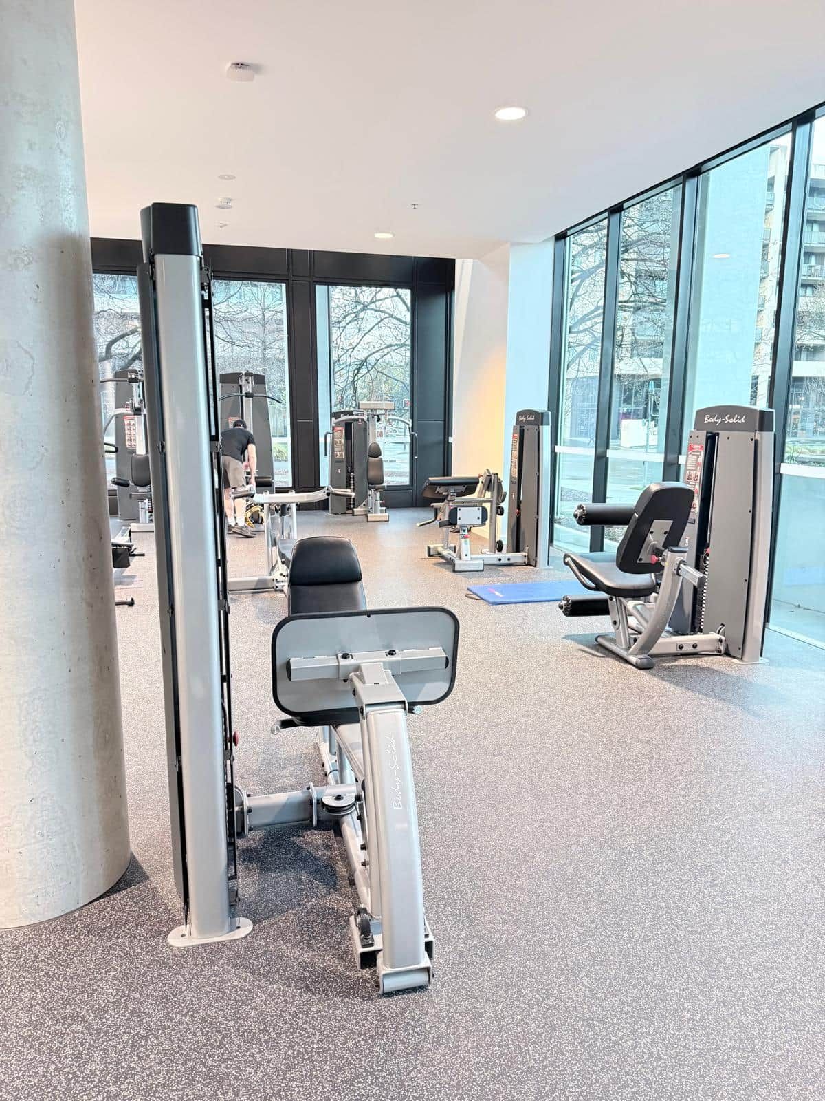 Een sportschool met diverse trainingsapparaten, grote ramen en uitzicht op het exterieur.