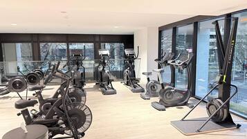 Academia moderna com diversas máquinas de cardio, uma janela ampla com vista para a cidade e uma lixeira identificada como 'WOWWipes'.