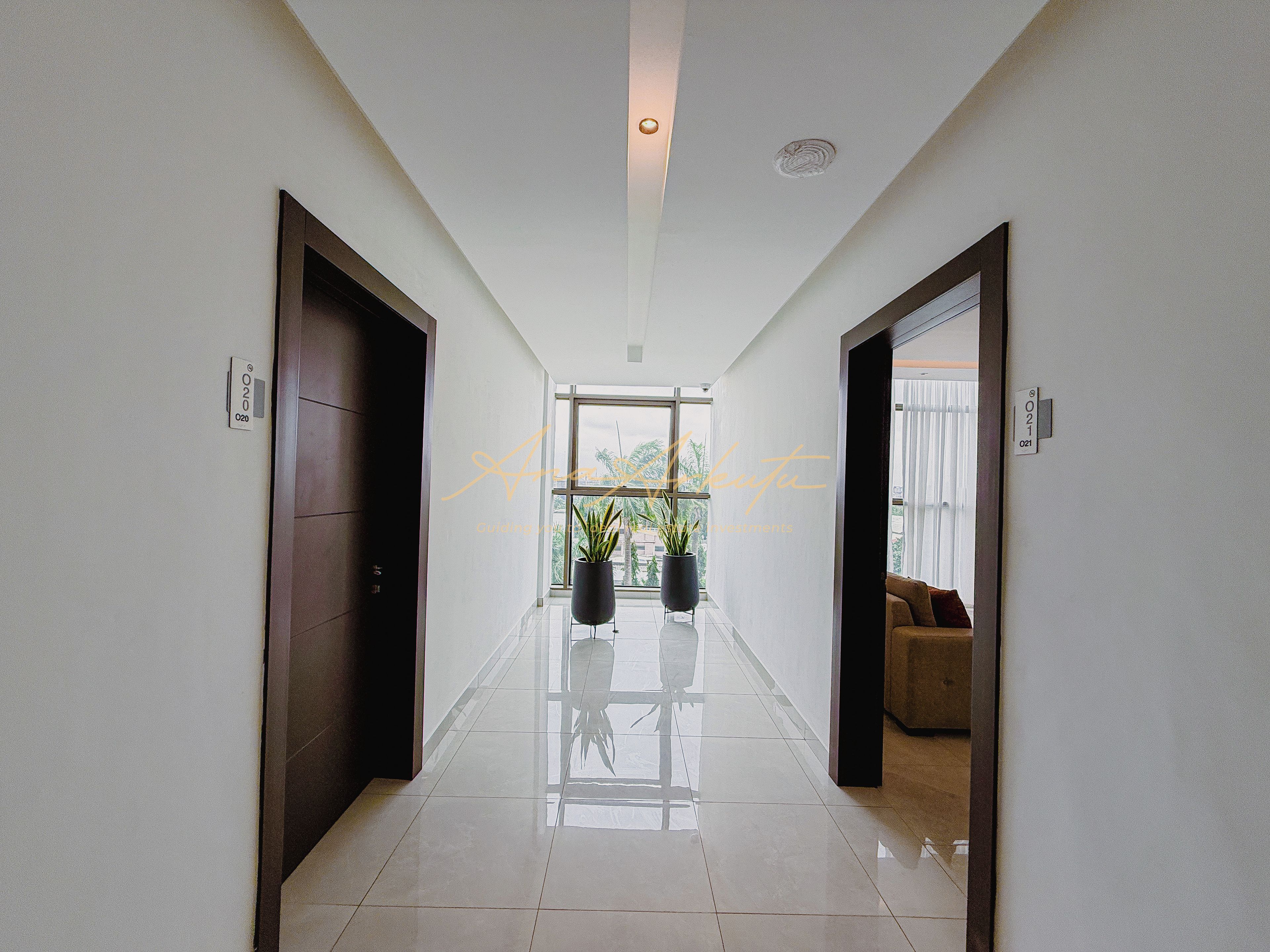 Un couloir au design moderne, avec une porte en verre au fond, une plante en pot et un canapé dans la pièce adjacente.