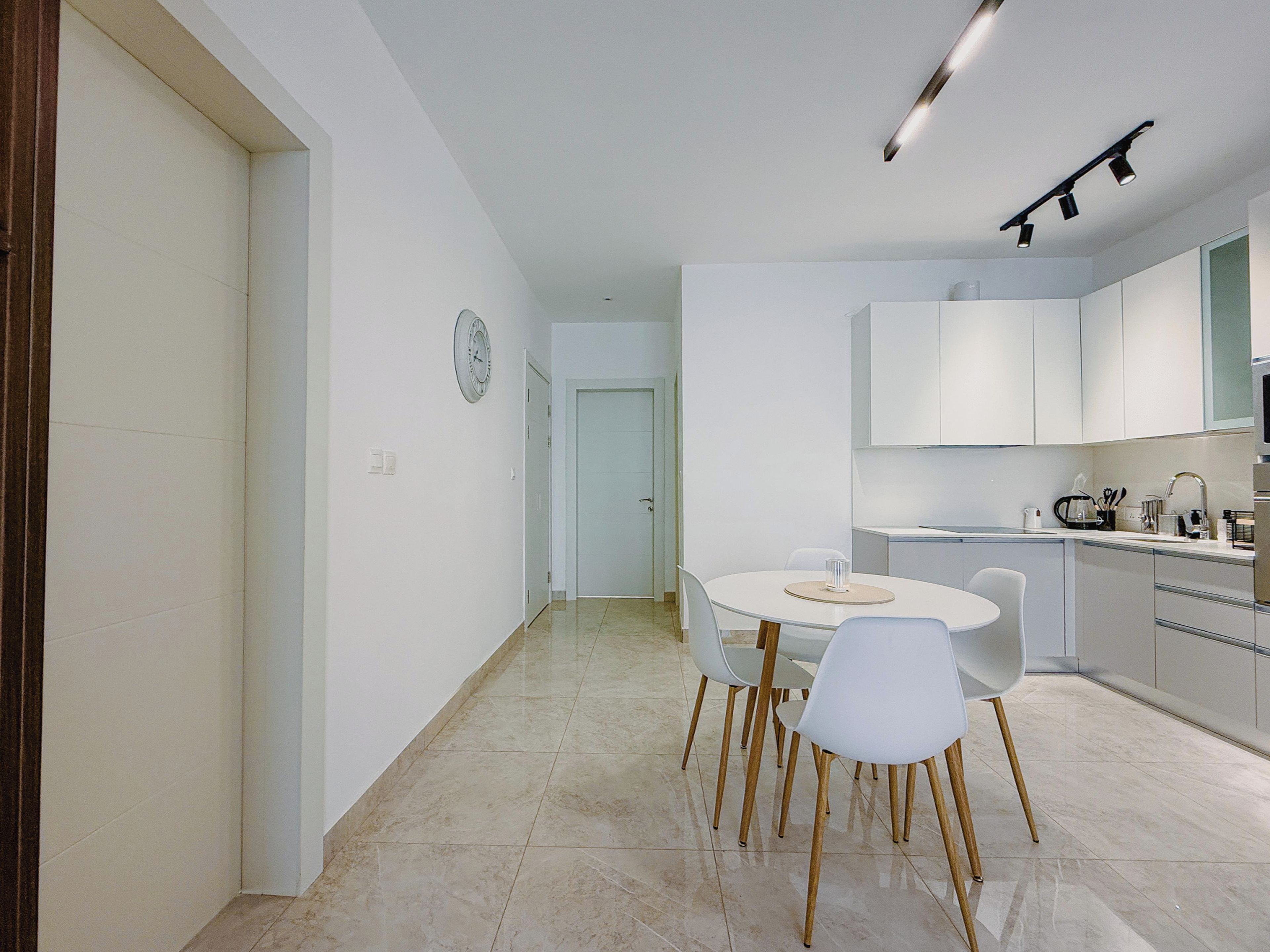 Une cuisine moderne avec des meubles blancs, une table à manger avec des chaises et une horloge au mur.