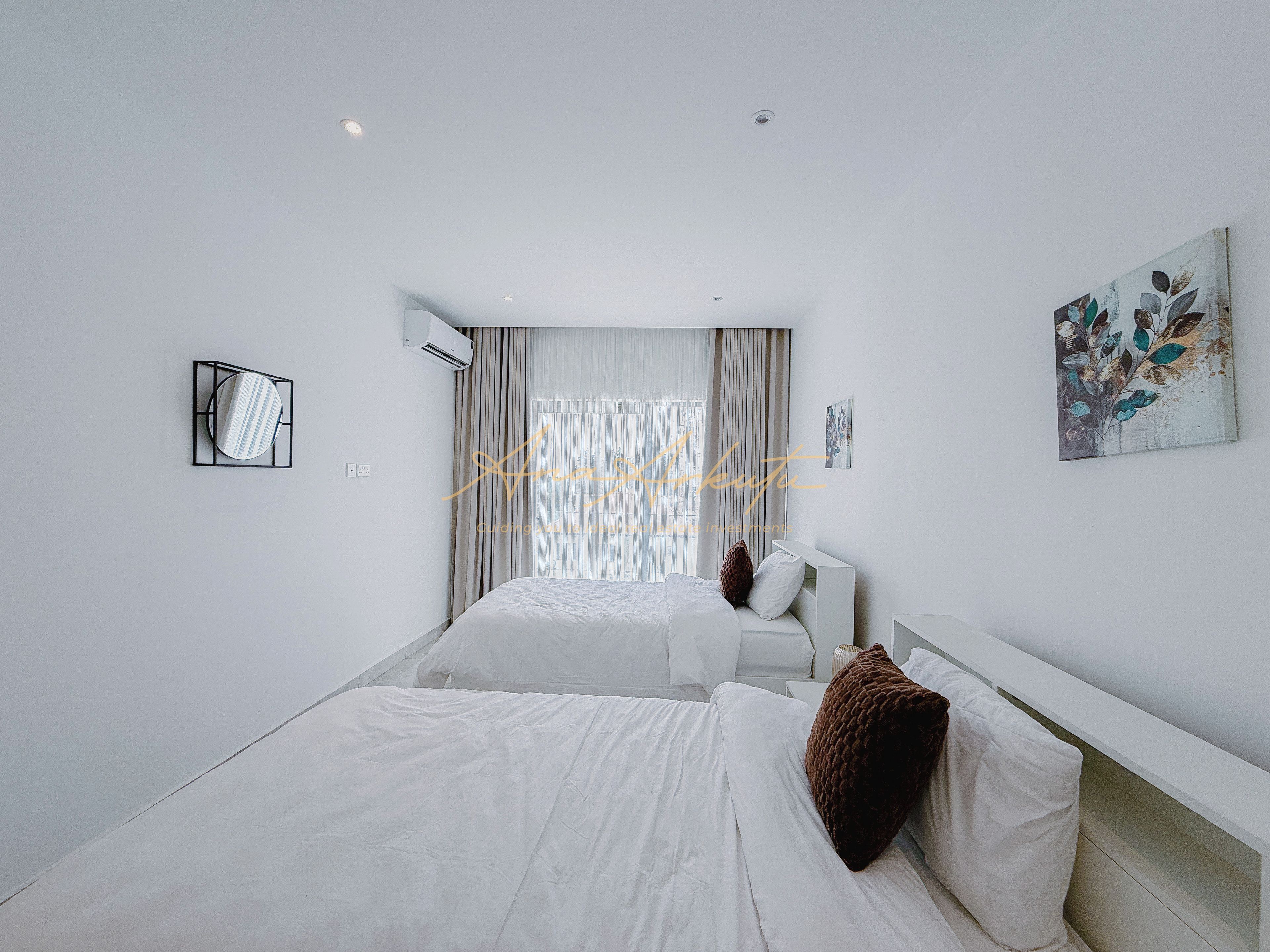 A hotel room with two beds, a large window with curtains, an air conditioning unit, and a wall-mounted artwork.