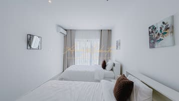 A hotel room with two beds, a large window with curtains, an air conditioning unit, and a wall-mounted artwork.