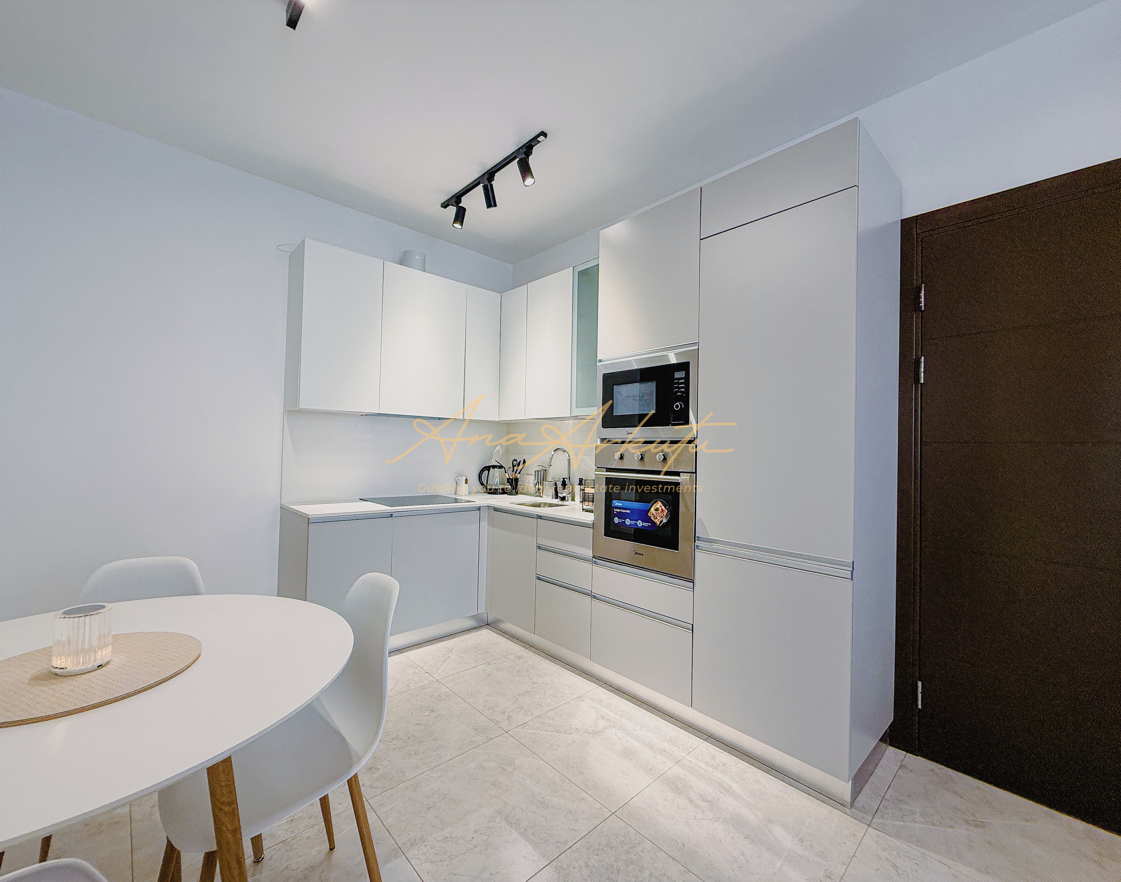 A modern kitchen with white cabinets, a built-in microwave, and a dining area with a round table and chairs.