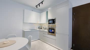 A modern kitchen with white cabinets, a built-in microwave, and a dining area with a round table and chairs.