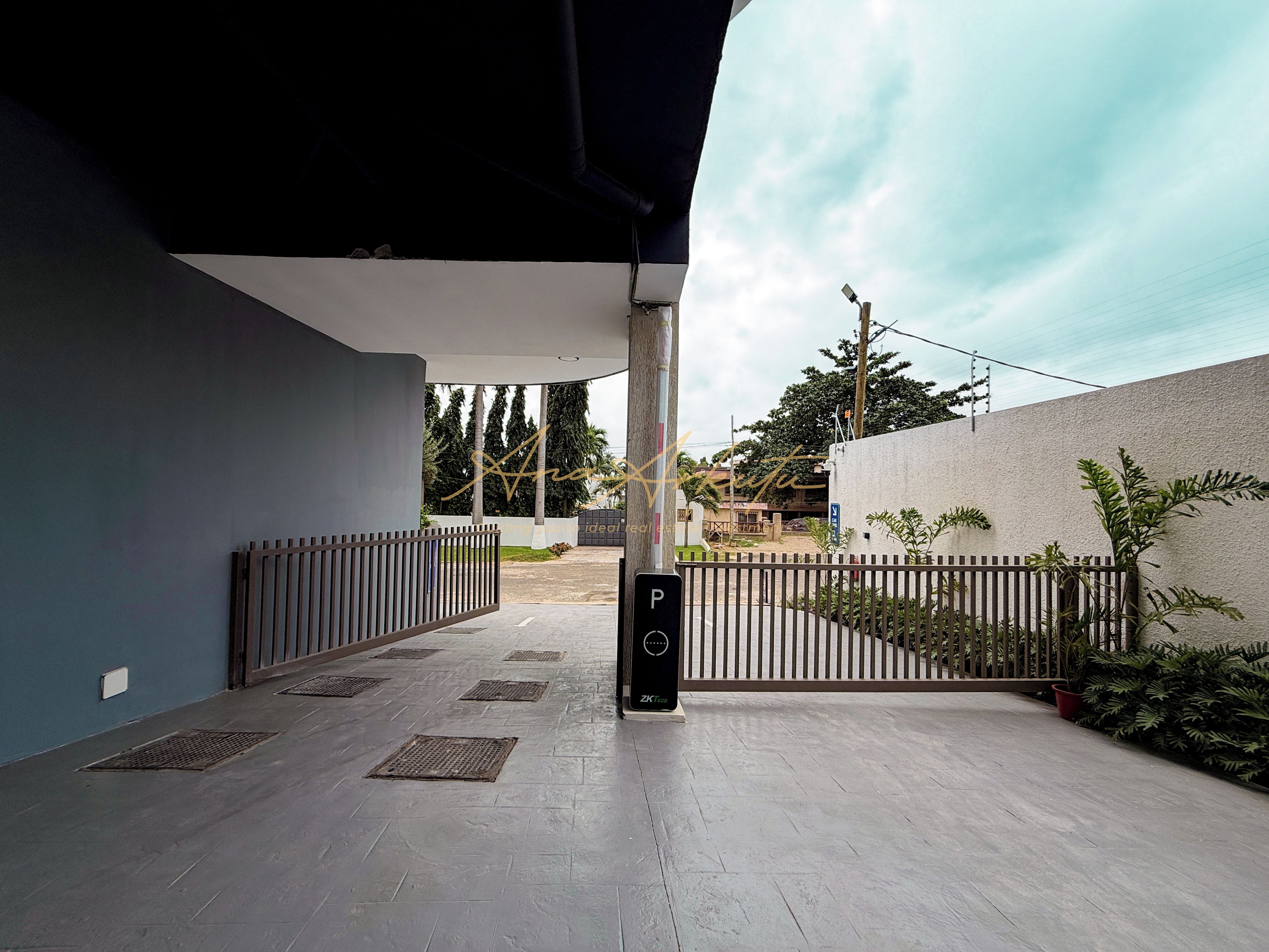 A covered outdoor area with a metal gate, a sign indicating a parking area, and a pathway leading to a building entrance.