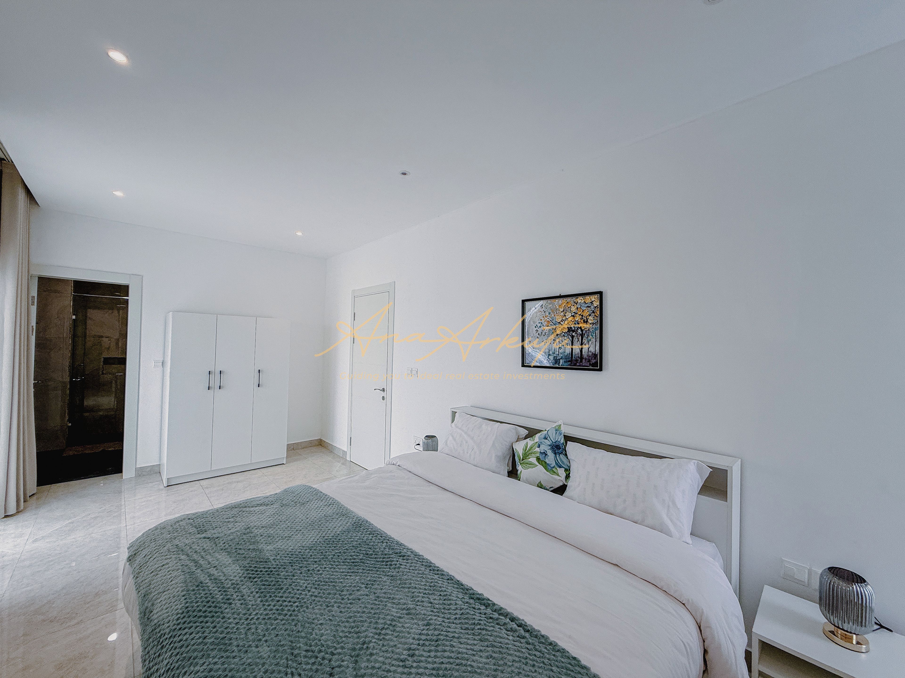 Une chambre à coucher moderne, avec un lit, une table de chevet, une lampe fixée au mur et une porte donnant accès à une salle de bain.