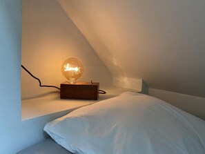 A single bed with a white pillow and a small table with a light bulb on it. - Maison la folie douce (Saint-Pierre-de-Manneville)