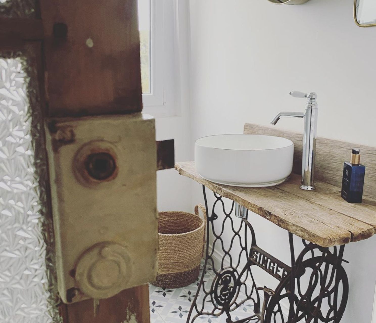 Een badkamer met een rond wit wastafel, een houten aanrechtblad, een metalen spoelbak en een gevlochten mand.