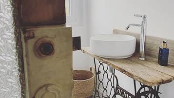 Een badkamer met een rond wit wastafel, een houten aanrechtblad, een metalen spoelbak en een gevlochten mand.