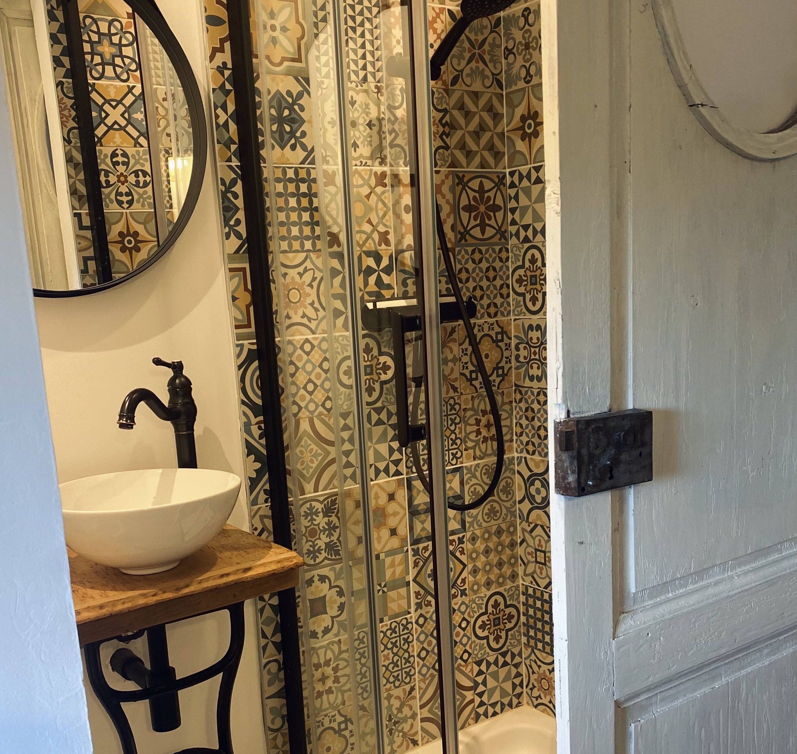 Un baño con un lavamanos blanco, un espejo y azulejos estampados.