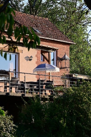 A brick building with a tiled roof, a balcony with outdoor furniture, and a large umbrella.