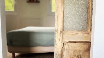 Une pièce comprenant un lit, une porte en bois avec un panneau texturé et une fenêtre donnant sur un paysage verdoyant.