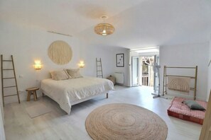 Ein Schlafzimmer mit einem Bett, einem runden Teppich, einem kleinen Hocker, einer Leiter und einer Tür zu einem Außenbereich.