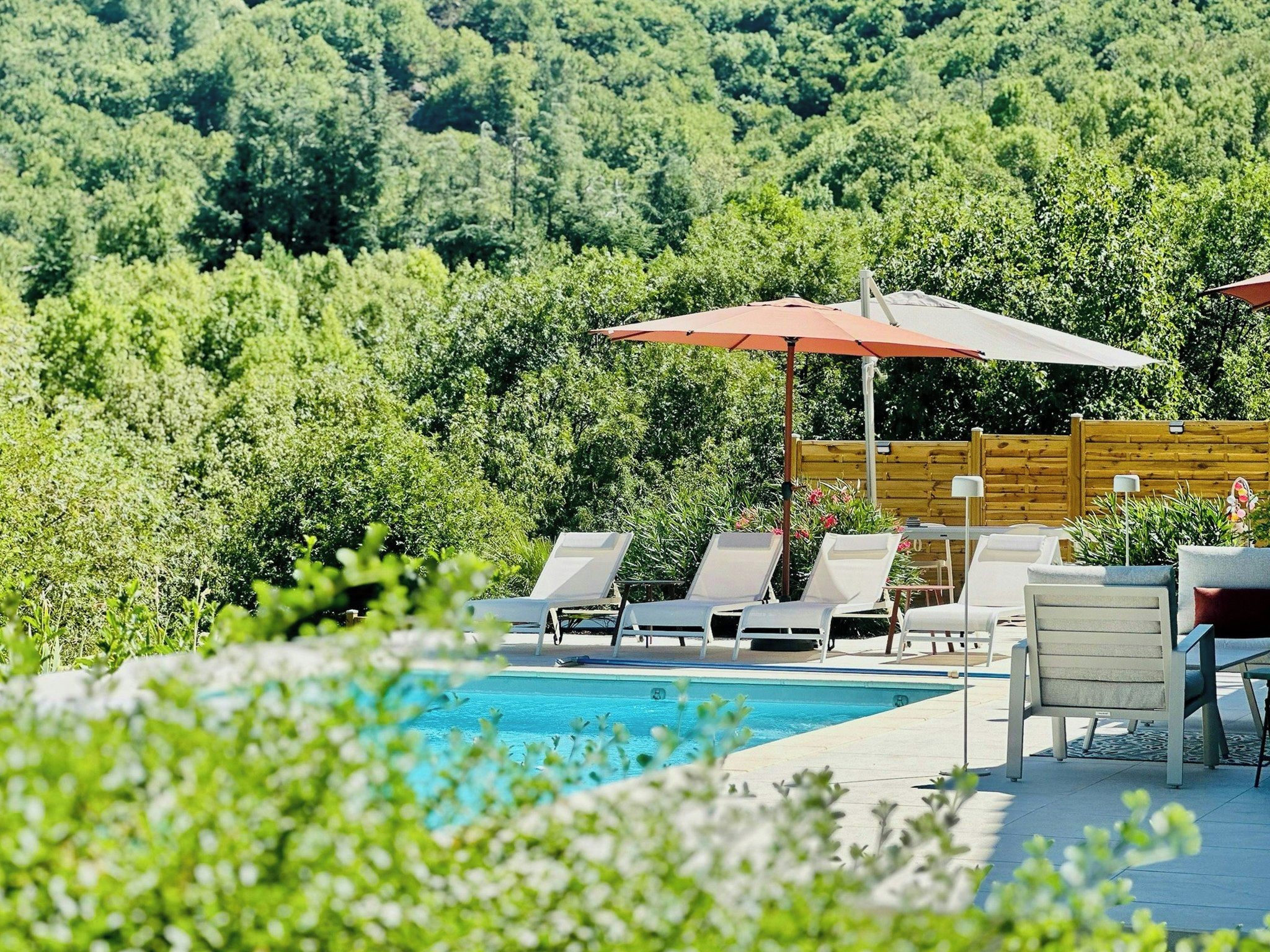 A pool area with lounge chairs and umbrellas, surrounded by greenery.