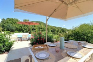 An outdoor dining area with tables set for two, surrounded by greenery and a pool. - Renovated stone house near Jaujac, Ardèche (Jaujac)