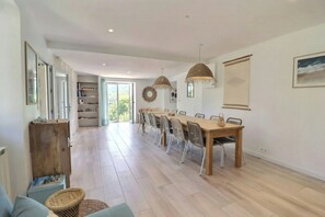 A spacious dining area with a long wooden table and chairs, a large window with a view of greenery, and a ceiling with recessed lighting. - Renovated stone house near Jaujac, Ardèche (Jaujac)