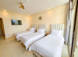 A hotel room with three single beds, a television on the wall, and a large window with curtains. - Vrbo Property (Tanger)