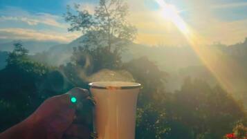 Una mano sostiene una taza con tapa transparente, con un paisaje montañoso y un amanecer de fondo.