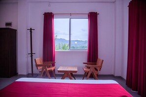 A room with a bed, two wooden chairs, a small table, and a window with curtains.