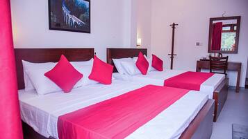 Habitación de hotel con dos camas, cada una con ropa blanca y almohadas rojas, cabecero de madera, mesita de noche con lámpara y un cuadro en la pared.