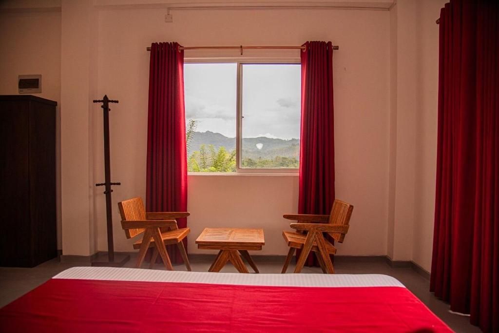 A room with a bed, two wooden chairs, a small table, and a window with red curtains.