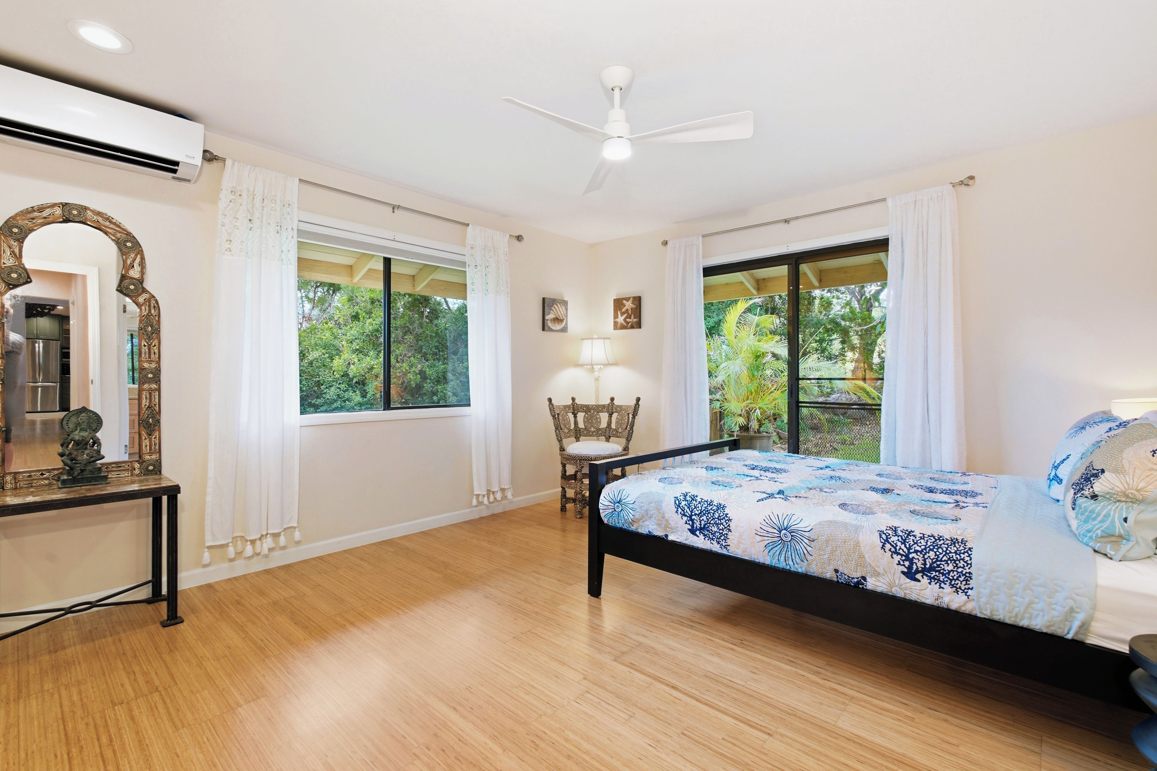 A bedroom with a bed, a chair, a table, a mirror, and a ceiling fan.
