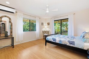 A bedroom with a bed, a chair, a table, a mirror, and a ceiling fan.