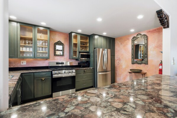 A kitchen with granite countertops, stainless steel appliances, and green cabinetry.