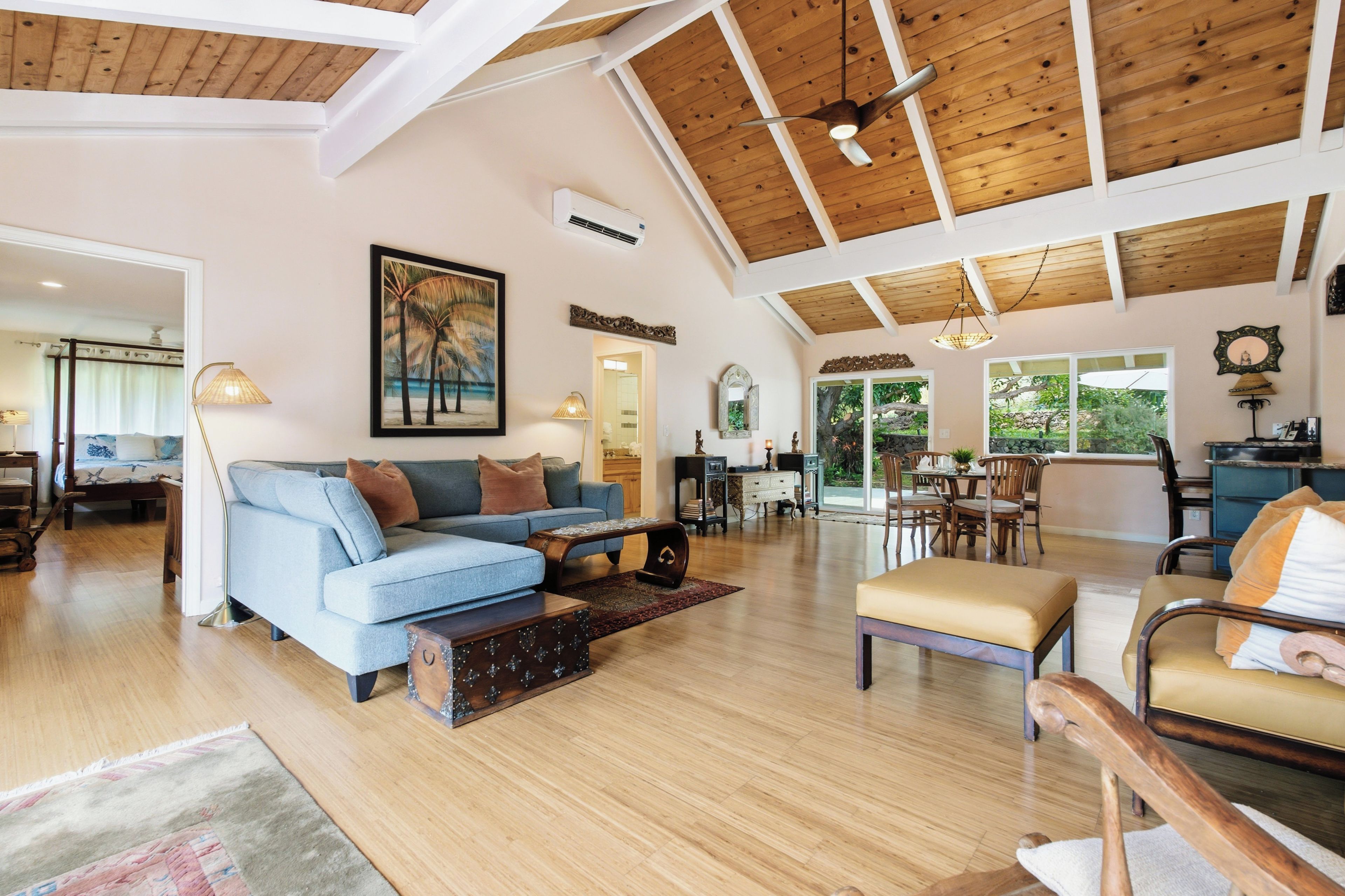 A spacious living area with a high ceiling, a blue sofa, a wooden coffee table, and a dining area with a table and chairs.