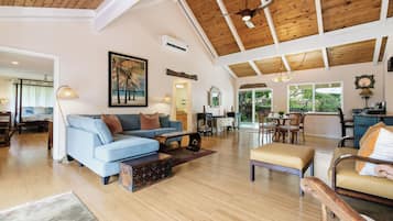 A spacious living area with a high ceiling, a blue sofa, a wooden coffee table, and a dining area with a table and chairs.