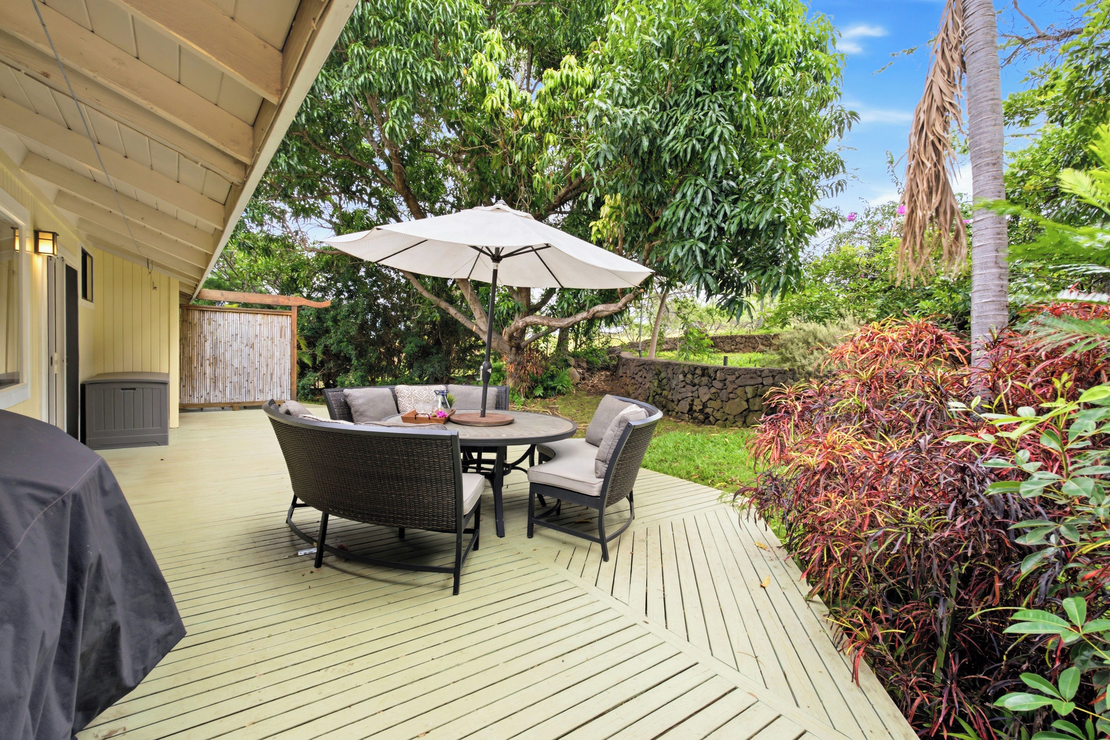 An outdoor patio with a round table and chairs, a large umbrella, and a wooden deck.