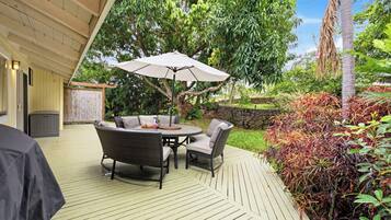 An outdoor patio with a round table and chairs, a large umbrella, and a wooden deck.